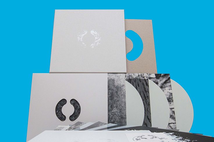 Rigid white linen-covered outer slipcase, clear foiled debossed graphic with die cut sleeves.